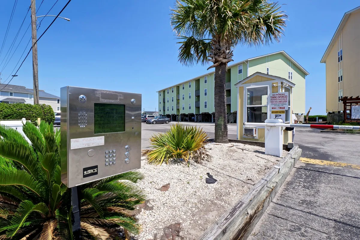 This exterior shot shows the entrance area of the property, surrounded by palm trees, parking space, and buildings. The entrance intercom and gathering area set a welcoming tone, suggesting easy access to the condo and a lively, community-oriented environment. The tropical landscaping reinforces the vacation atmosphere.