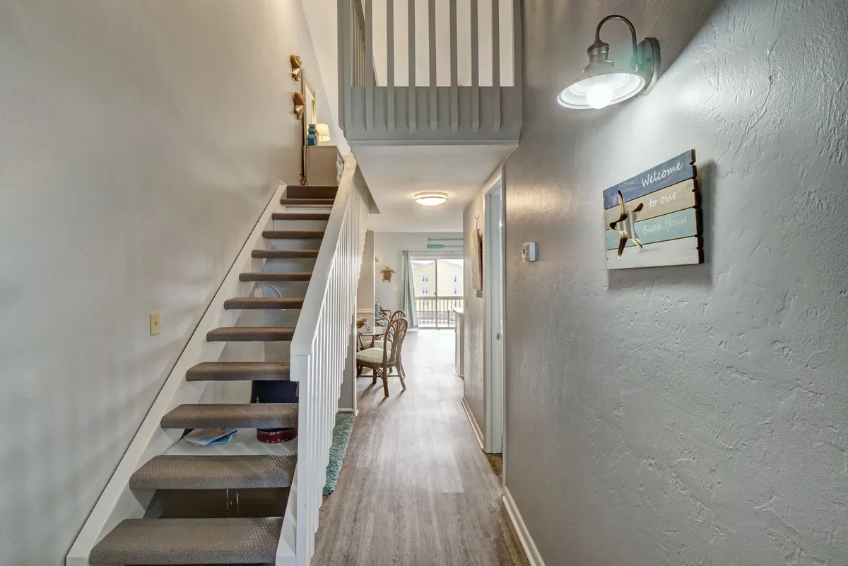 This image captures the inviting entryway, showcasing a stylish staircase, decorative wall signs, and a glimpse of the dining area in the background. Natural light fills the space, creating an airy and welcoming atmosphere, ideal for setting the scene as couples arrive for their coastal escape.