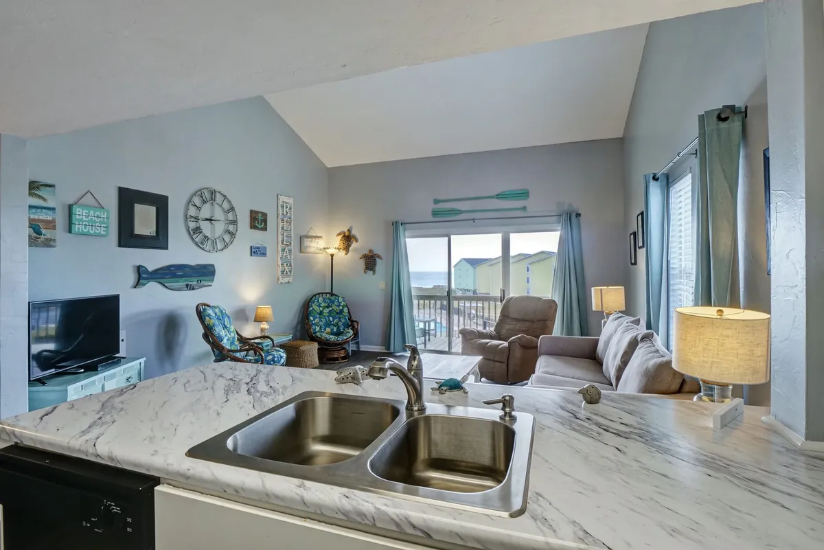 A bright living space combining a comfortable seating area, marble kitchen counter, large windows with views, and curated wall art. The room feels both cheerful and intimate, ideal for family time or entertaining.
