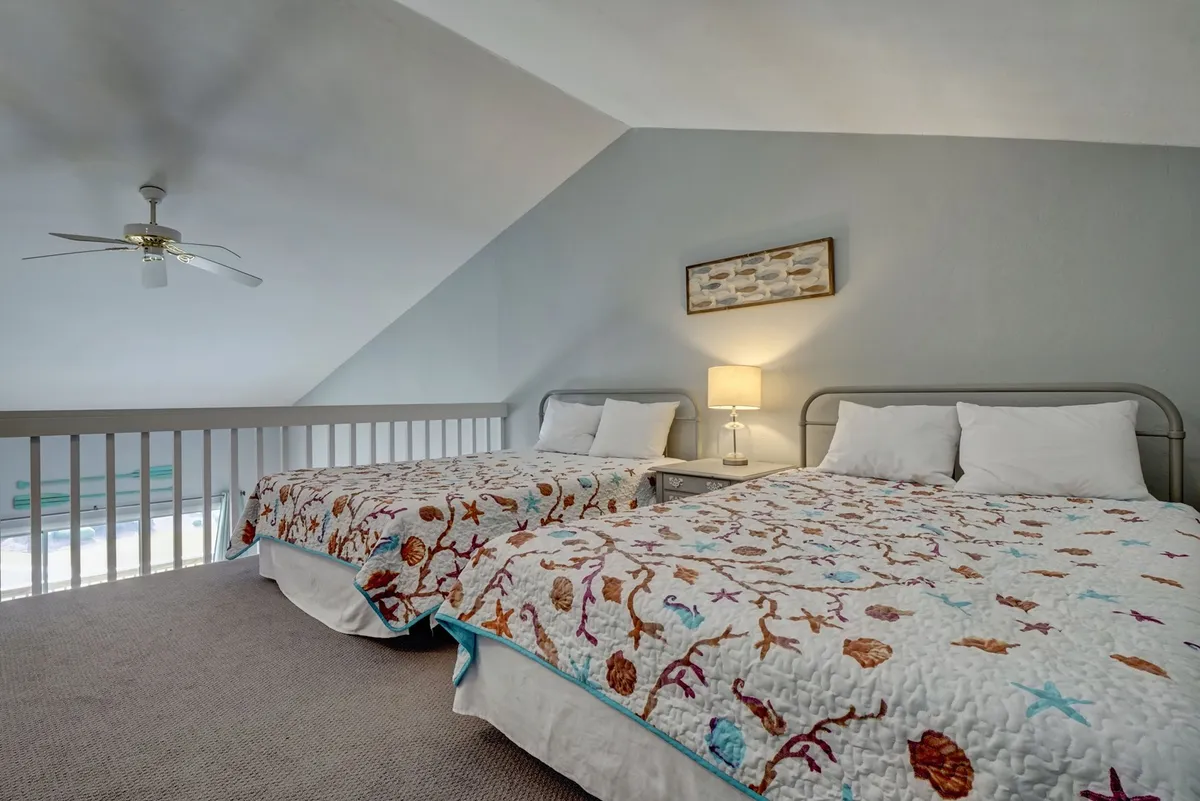 A spacious bedroom with two beds adorned in vibrant quilts, a shared bedside table with a lamp, and decorative wall art. The room feels relaxed and is ideal for families or groups, offering a cozy and inviting ambiance.