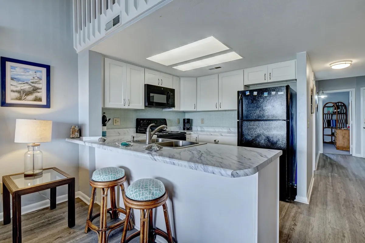 A bright, modern kitchen featuring a spacious island with bar stools, sleek new cabinetry, contemporary appliances, and artistic wall decor. The open layout encourages socializing and creating meals together.