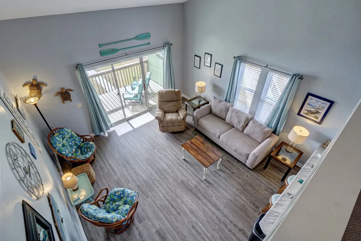 A cozy living area with plush seating, decorative chairs, a central coffee table, and a large sliding glass door that leads out to a private deck. Warm textures and decorative touches create a relaxed setting.